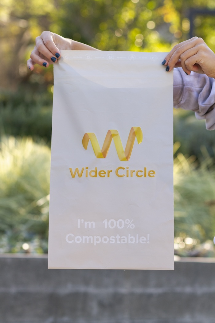 “I’m 100% Compostable” text on a padded mailer with a custom Wider Circle logo and name being held up, produced and shipped by Swagger.