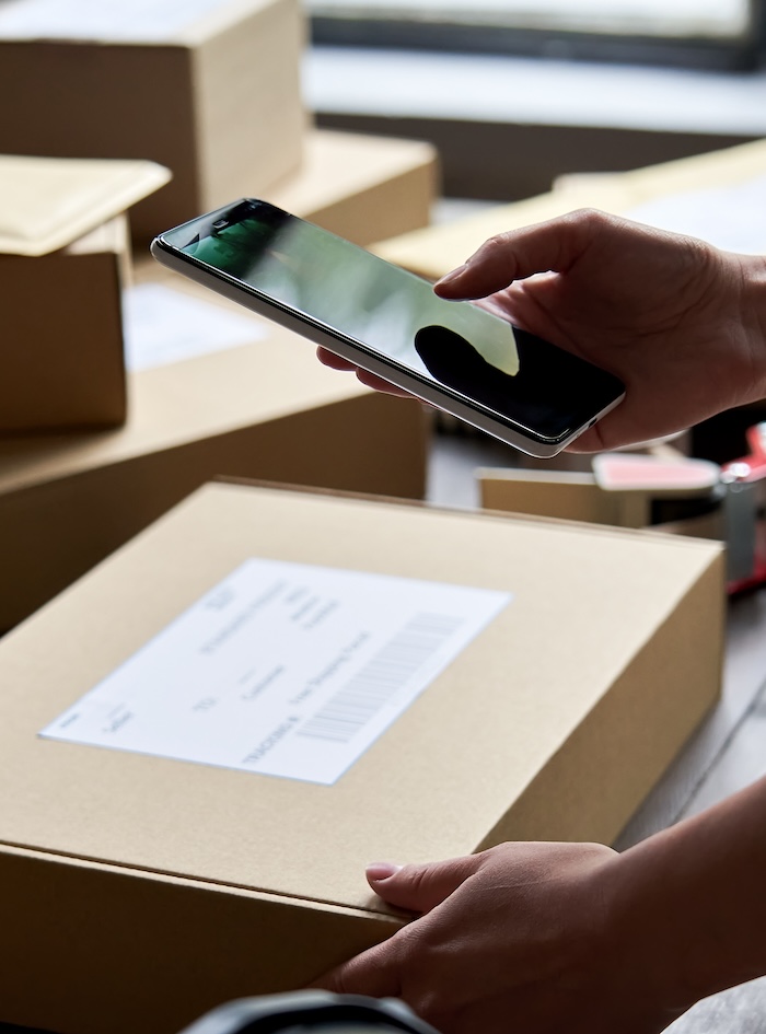 Swagger employee placing shipping label on custom swag box and using her mobile phone to mark off inventory. See other boxes and padded mailers in the background that Swagger is preparing for clients.
