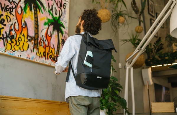 Man standing in front of a painting wearing the Moleskine® Metro Rolltop Backpack designed by Swagger.