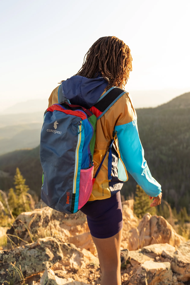 Person hiking in Cotopaxi multi-color Batac 16 backpack curated by Swagger