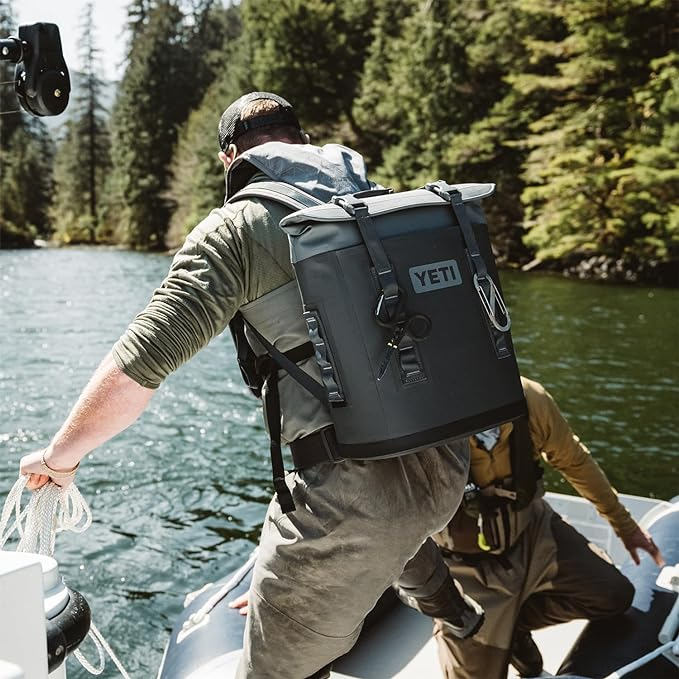 Two people fishing in a boat on a river with the YETI M12 Backpack Soft Cooler, can be custom branded by Swagger.