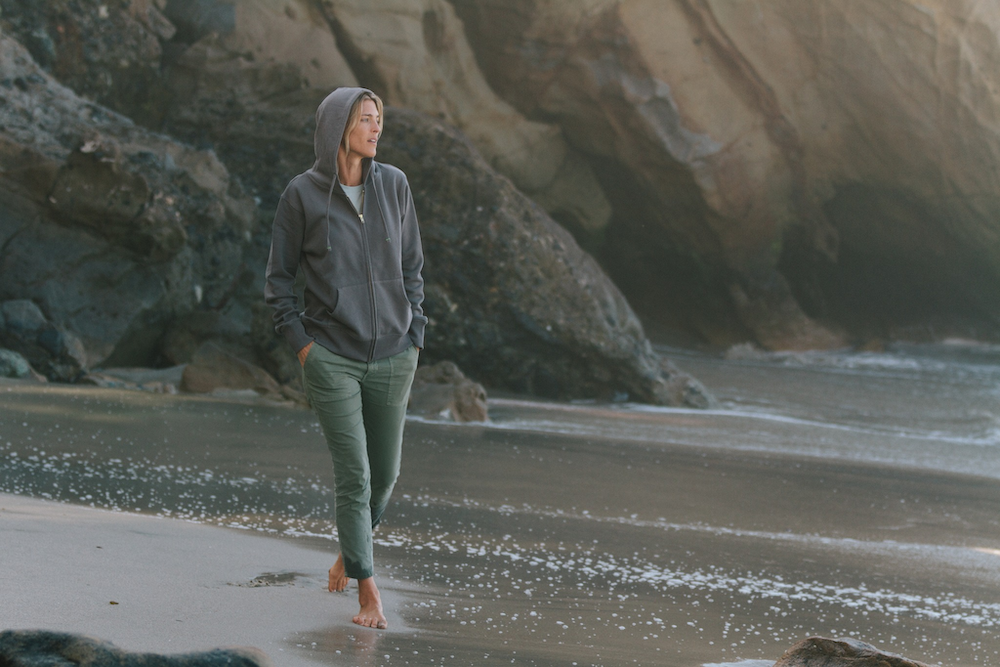 Woman walking on the beach wearing the Econscious Organic/Recycled Full-zip Hooded Sweatshirt designed by Swagger.
