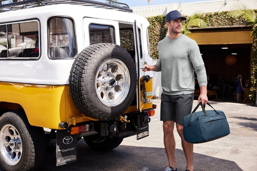 A man standing by a Jeep holding a TravisMathew overnight bag and hat curated by Swagger.