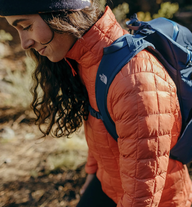 Girl hiking and showcasing custom swag: North Face backpack and quilted North Face jacket, curated by Swagger.